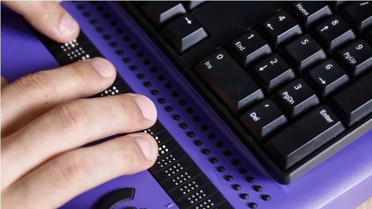 Manos usando teclado y pantalla braille, reflejando accesibilidad en diseño web.